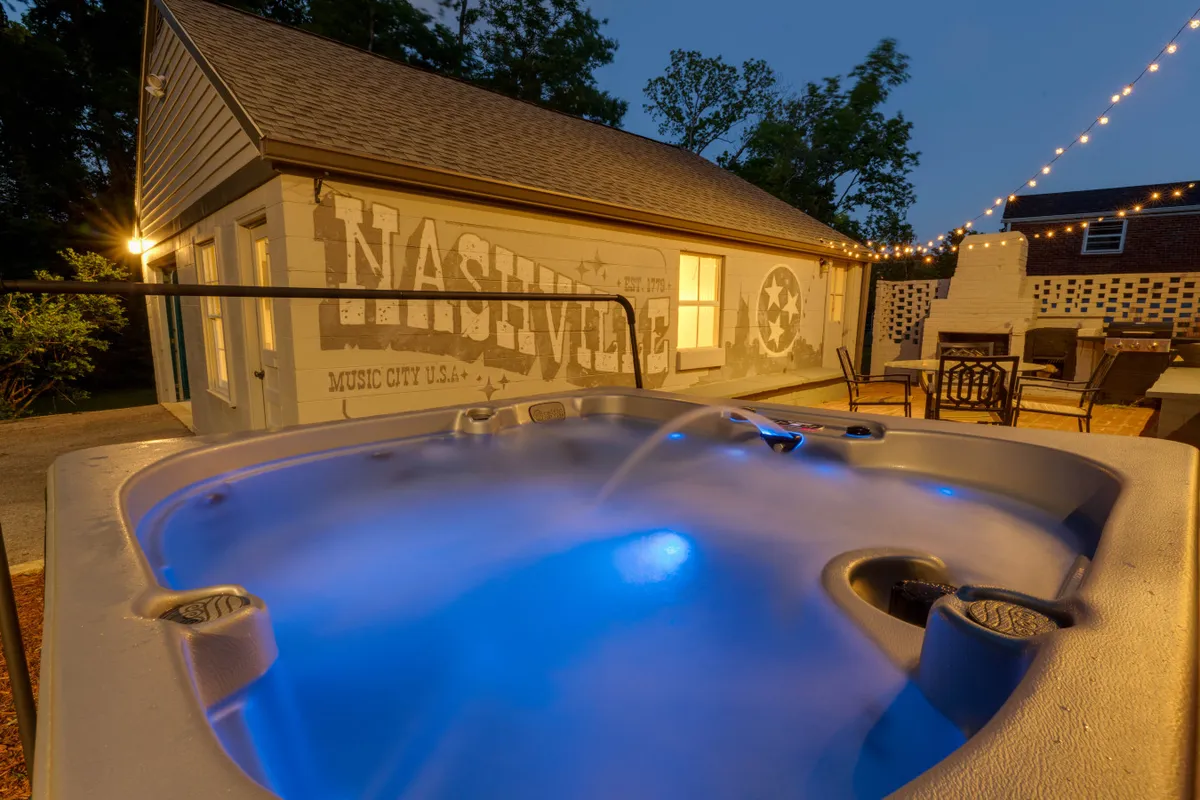 A cozy evening deck scene with a glowing blue-lit hot tub, modern outdoor seating, and a striking Nashville mural. Guests can be seen unwinding, capturing the mood of immersive relaxation and social connection against the backdrop of city-inspired art.