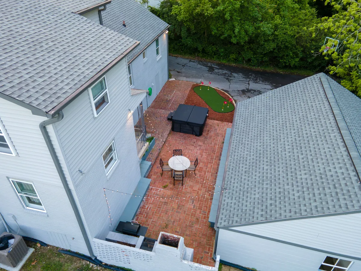 This outdoor scene features a patio table and chairs, sleek black outdoor furniture, a putting green, and lush greenery surrounding the area. The setup is ideal for outdoor dining, group conversations, or playful team activities in a relaxed, natural environment.