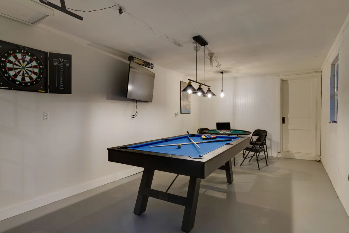 An interior game room featuring a pool table, dartboard, television, and hanging lights. The mood is relaxed and entertaining, with clear indications of spaces designed for friendly competition and group fun.