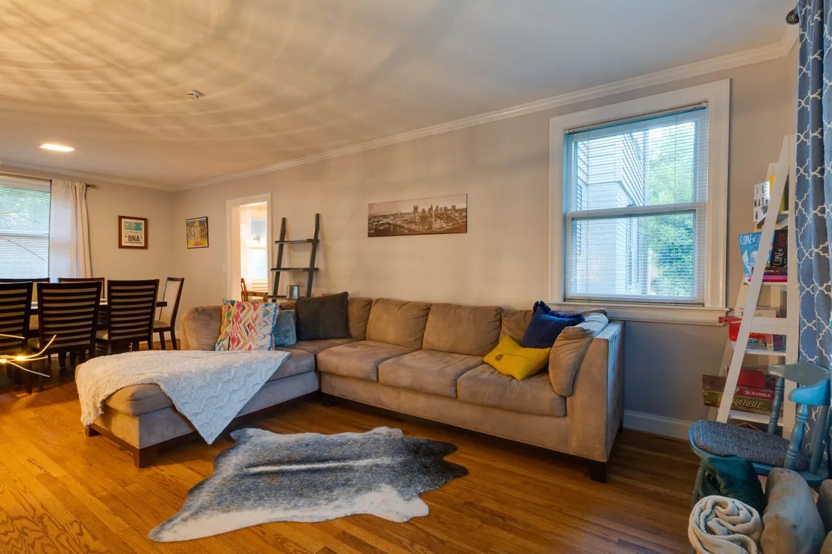 This image showcases a cozy open-concept living and dining space with a sectional sofa, a dining table, and warm artwork on the wall. Soft throw blankets add to the inviting atmosphere, making the area ideal for relaxing, socializing, or enjoying a group meal.