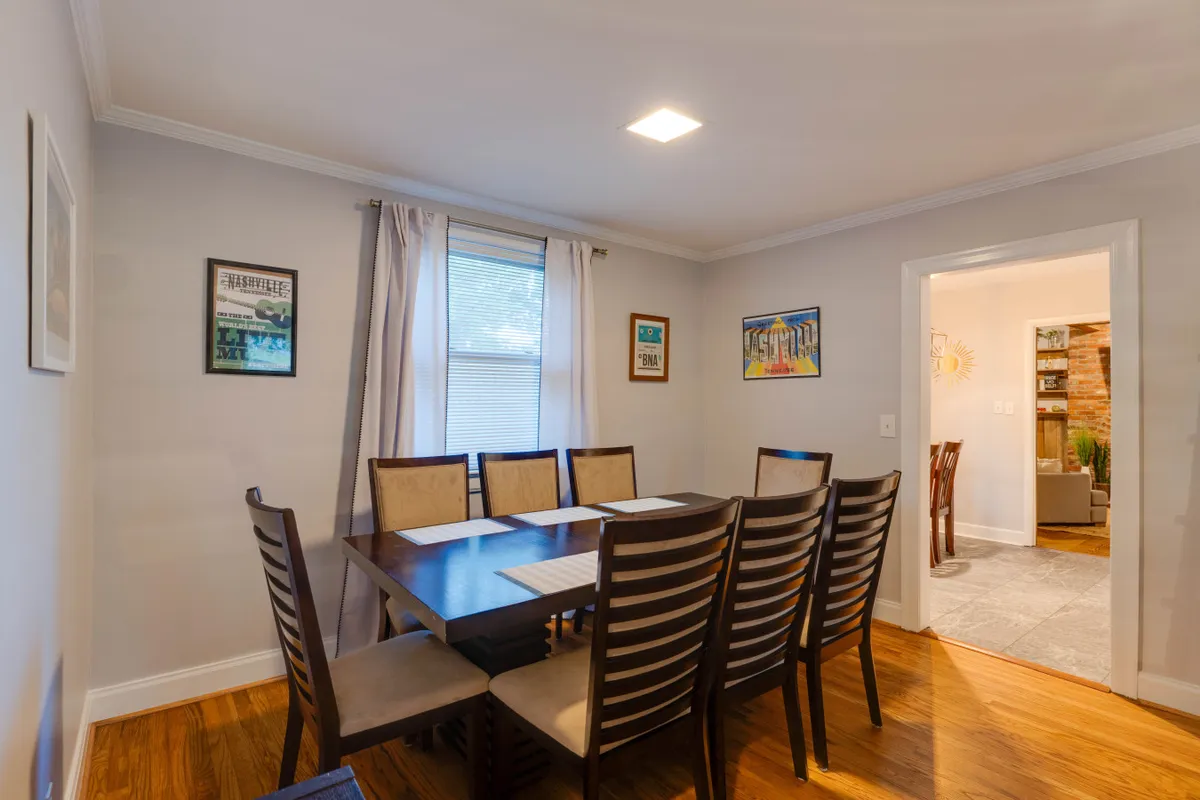 An inviting dining area with a large table, comfortable chairs, and artwork adorning the walls. Bright natural light filters through the window, setting the scene for family dinners, holiday gatherings, or casual entertaining with friends.
