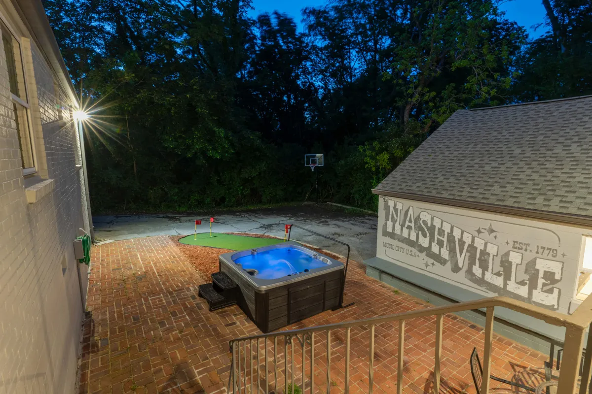 This vibrant exterior shot captures the backyard entertainment complex, featuring a hot tub, a colorful Nashville mural, basketball hoop, and a putting green area. The space is designed for active play, relaxation, and family fun.