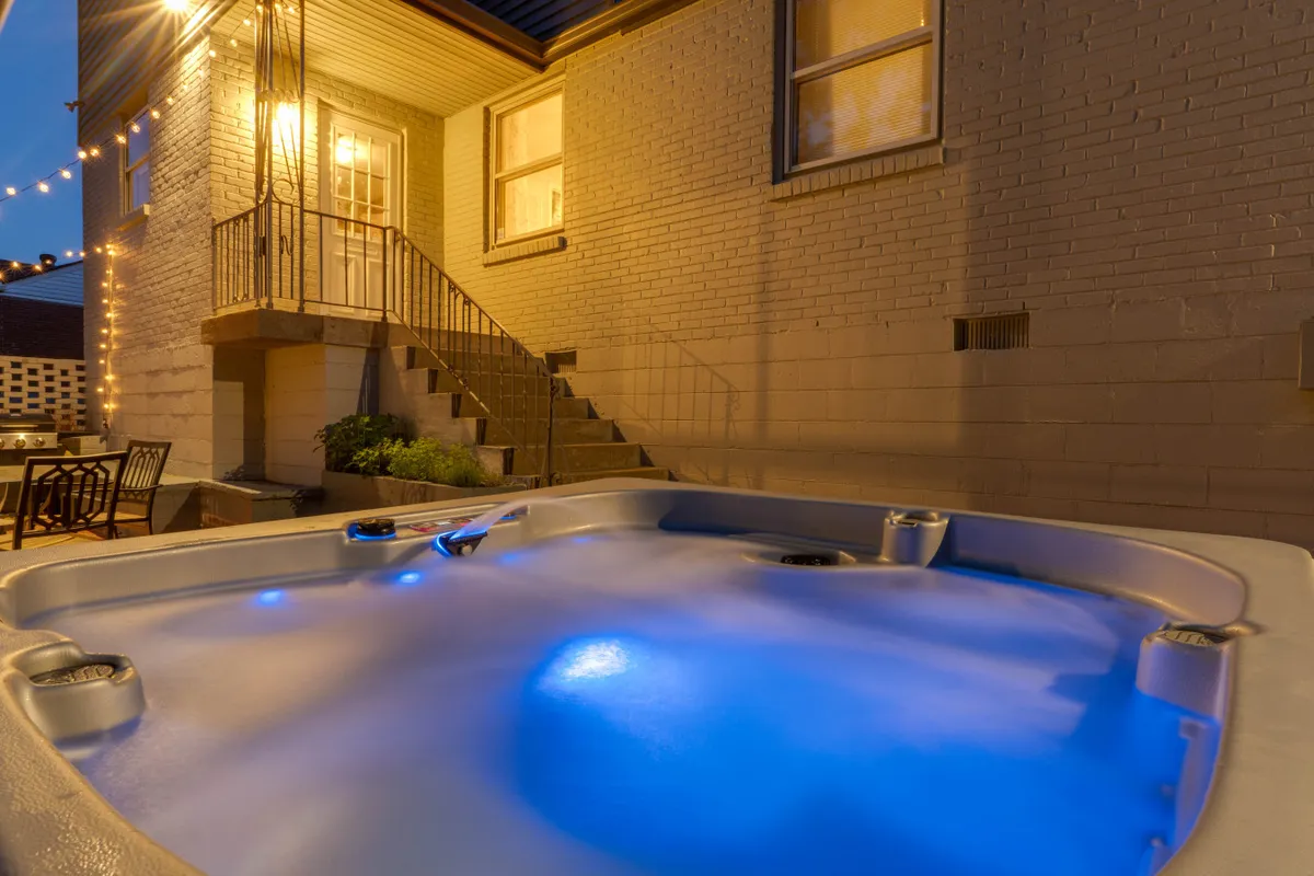 This tranquil scene highlights the hot tub with glowing blue lights, an inviting outdoor seating area, and a staircase leading into the home, suggesting a seamless flow between indoor and outdoor spaces. The setting feels intimate and ideal for stargazing or quiet evening chats.